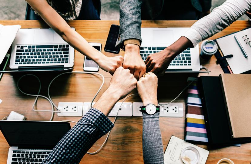 group of workers fist bumping over a desk of computers